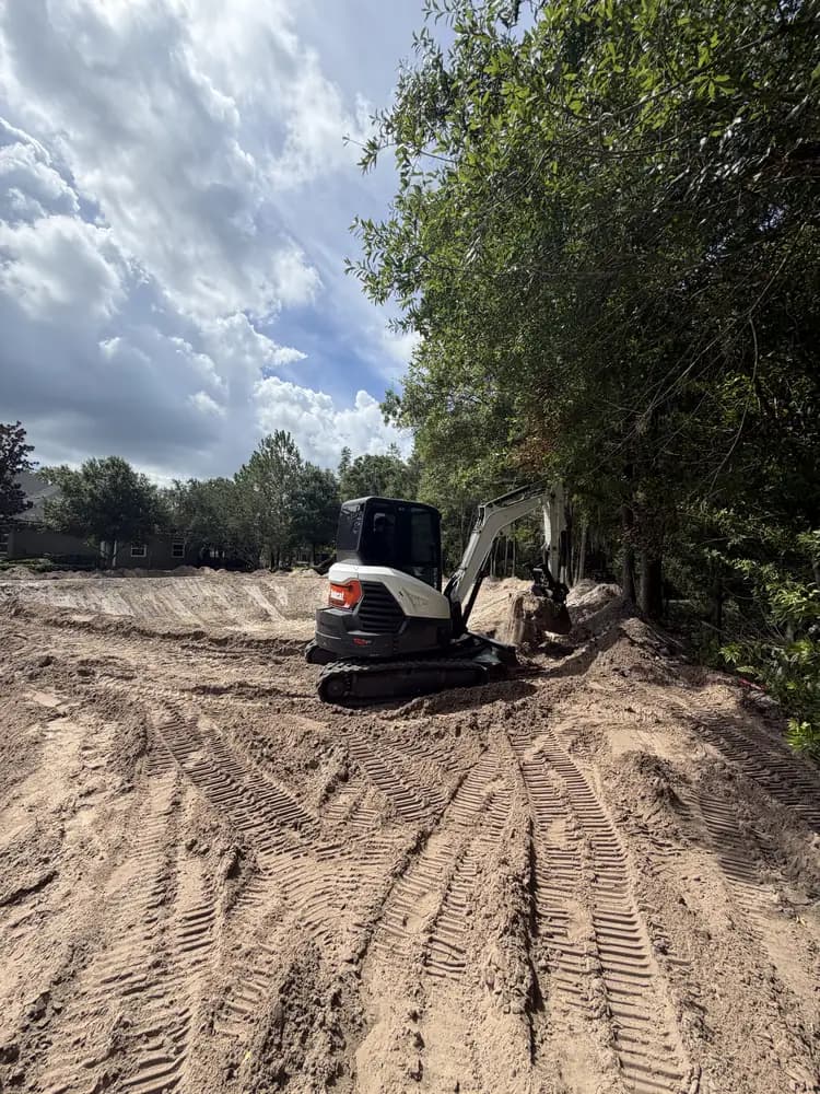 Mini excavator regrading a sand shoreline next to the water