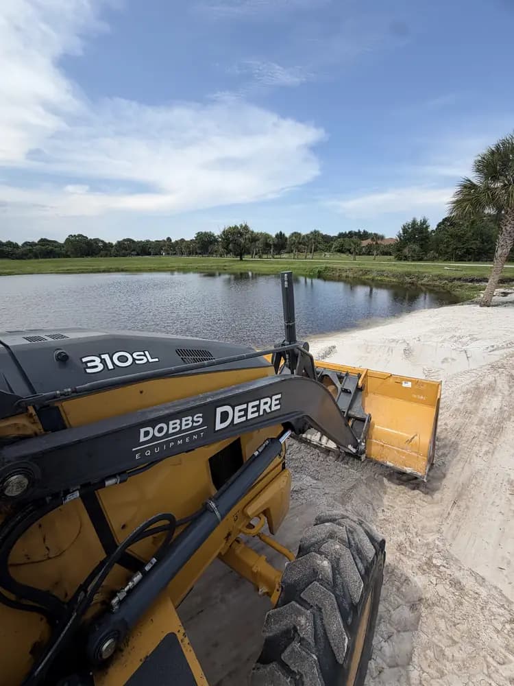 Excavator grading a new sand shoreline along the water's edge